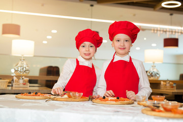 Wall Mural - two beautiful cook girls in white shirts and red aprons in the restaurant make pizza