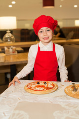 Wall Mural - beautiful little girl cook in a red apron with pizza