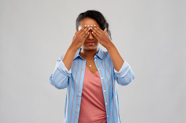 people, emotion and expression concept - african american young woman with eyes closed by hands over grey background