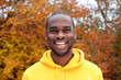 © mimagephotos - Close up handsome young black man smiling against autumn leaves in background