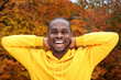 © mimagephotos - handsome young african american man smiling with autumn leaves in background and hands behind head