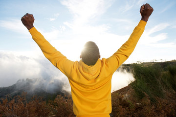 Wall Mural - back of black man in hoodie with hands raised in air and sun in background