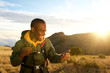 © mimagephotos - smiling young man hiking in mountains and looking at cellphone