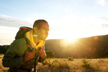 Wall Mural - Side of african american man hiking in mountains with sunset in background