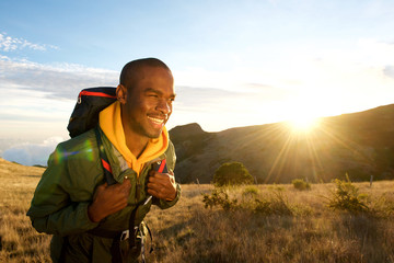 young black man walking with backpack in mountains with sunrise in background