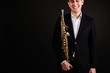 Man saxophonist in black classic suit holding a soprano saxophone standing on a black background