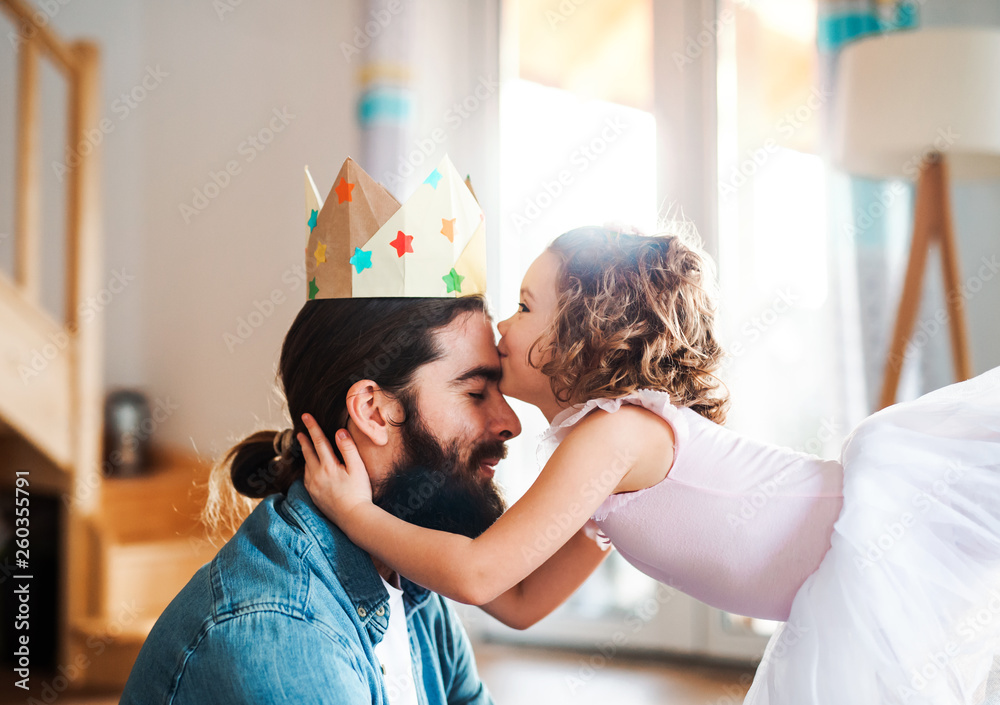 A side view of small girl with a princess crown and young father at home, playing. - obrazy, fototapety, plakaty 