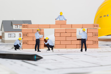 Small architects building model house construction with brick on blueprint.