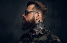 Profile Of A Stylish Bearded Guy With Tattooed Hands In The Military Shirt. Studio Photo Against Dark Wall