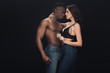 © LIGHTFIELD STUDIOS - beautiful sexy woman embracing shirtless african american man and holding condom isolated on black