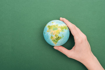 partial view of woman holding toy earth on green background with copy space