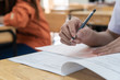© smolaw11 - School / university Students hands taking exams, writing examination room with holding pencil on optical form answers paper sheet on desk doing final test in classroom. Education assessment Concept