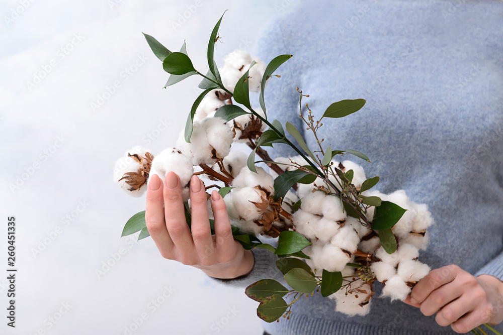 Woman holding floral composition with cotton flowers on light background