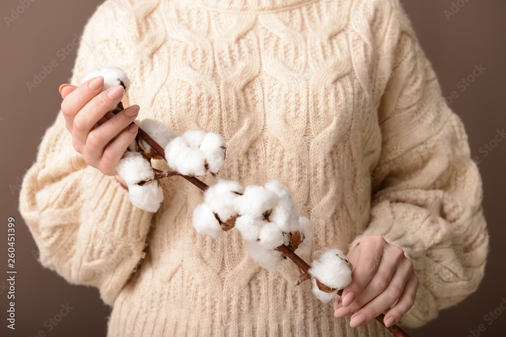 Woman holding cotton flowers on color background