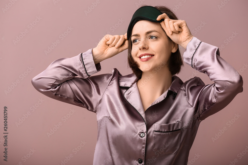 Young woman with sleep mask on color background
