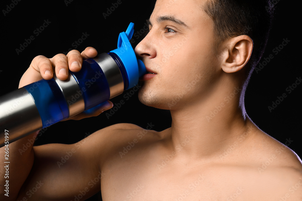 Sporty man drinking protein shake on dark background