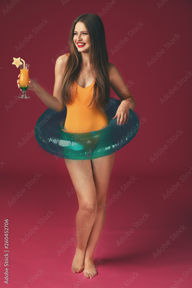 Beautiful young woman with inflatable ring and cocktail on color background