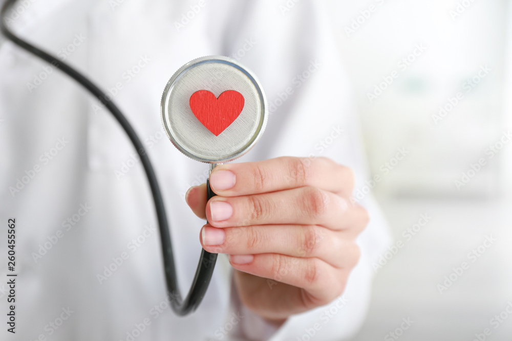 Cardiologist holding stethoscope with red heart in clinic, closeup
