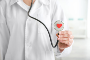 Cardiologist holding stethoscope with red heart in clinic, closeup