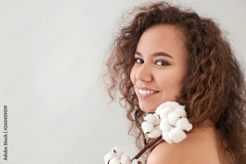 Beautiful young woman with cotton branch on light background