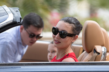 beautiful rich brunette girl in a red dress behind the wheel of a car