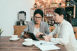 © PR Image Factory - office ladies business cooperation meeting teamwork concept. Two businesswomen talk chat sitting at table in cafe shop. Girl in suit shows colleague information on tablet screen working in coffee bar