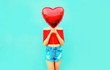 Happy woman hides her head holding in hands red heart shaped air balloon having fun on colorful blue background
