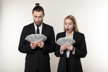 Portrait of couple in black suits shocked holding money banknotes in hands