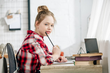 Canvas Print - Pensive teenager in checkered shirt holding pen at table while doing homework