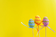 Easter Purple, Yellow And Blue Decorated Eggs Stand On A Wooden Sticks On Yellow Background. Minimal Easter Concept. Happy Easter Card With Copy Space For Text.