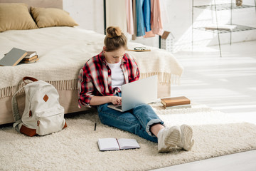 Wall Mural - Teenager with laptop and books sitting on carpet and doing homework