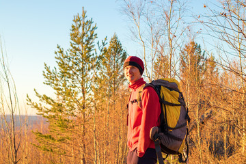 man backpacker stands in forest at sunset in fall in yellow trees