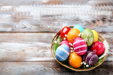 Colorful Easter Eggs In Basket With Gypsophila Flowers On Brown Wooden Table