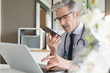 © goodluz - Handsome doctor talking on cellphone in modern office