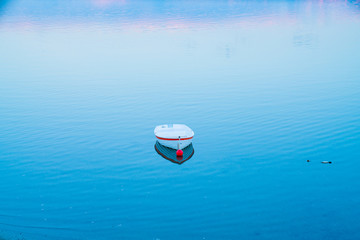 Sticker - White dinghy afloat on calm blue water with reflection of sunset colors