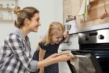 Canvas Print - Mother and her daughter baking food in oven at home