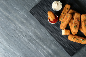 Board with cheese sticks and sauces on table, top view. Space for text