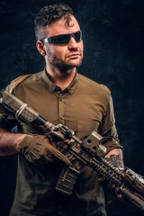 Wall Mural - Portrait of a stylish man wearing shirt sunglasses holding assault rifle and looking sideways.