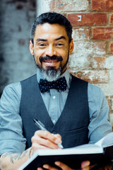 Wall Mural - Smiling man in bow tie holding pen and notebook, writing