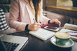 © Elizaveta - Close up caucasian woman hand on wooden table inside cafe makes notes in notebook. Subject freelancer blogger journalist at work. Unrecognizable person. Technology phone and laptop with cup coffee