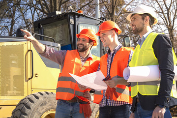 male workers engineers in helmets are watching the drawings near the bulldozer and excavator