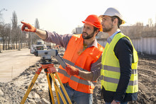 Two Male Surveyor Engineer With A Device Working On A Construction Site In A Helmet