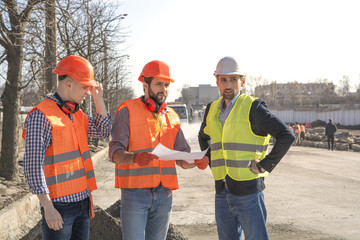 male builders workers engineers at a construction site looking drawings in helmets