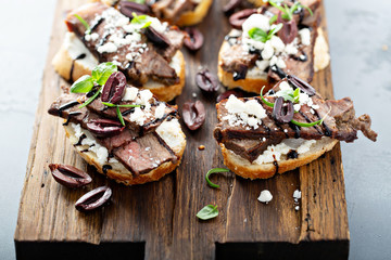 Wall Mural - Steak bruschetta or crostini with beef, olives and feta cheese on a cutting board