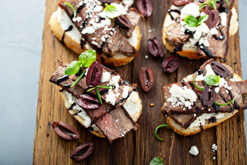 Wall Mural - Steak bruschetta or crostini with beef, olives and feta cheese on a cutting board