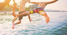 Group Of Happy Crazy People Having Fun Jumping In The Sea Water From Boat. Friends Jump In Mid Air On Sunny Day Summer Pool Party At Diving Holiday. Travel Vacation, Friendship, Youth Holiday Concept.