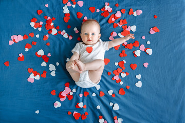 cute adorable white caucasian baby girl boy infant with blue eyes four months old lying on bed among