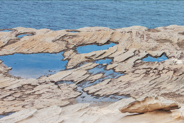 Clifftop rock with stone and reflected sky on puddles