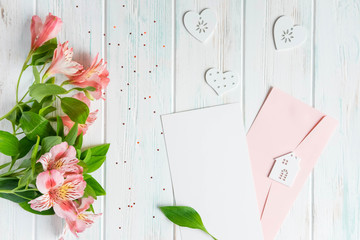 Mock up blank paper and envelope on dark wooden background with natural flowers of white color. Blank, frame for text. Greeting card design with flowers. Aalstroemeria background. Flat lay, top view.