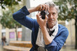 © goodluz - Mature photographer taking photos on with vintage camera in old town